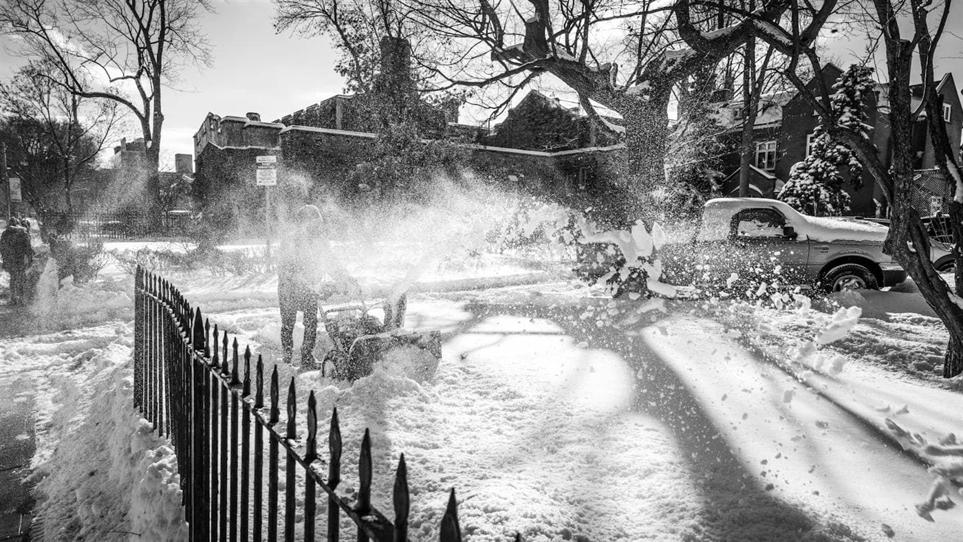 A person clearing snow from a residential driveway with a snowblower