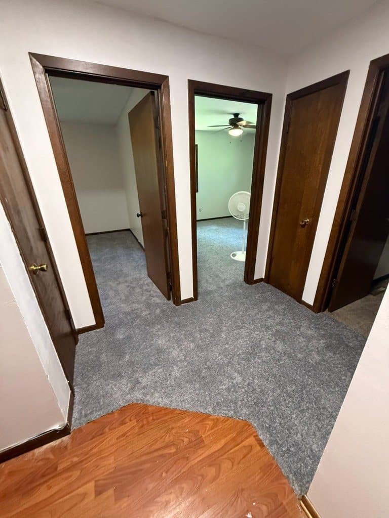 Gray carpet in an upstairs hallway with open doorways and wood trim