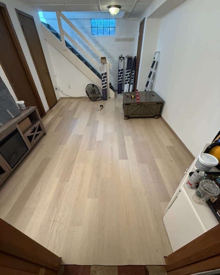 Light wood-look vinyl plank in a basement family room, with stairs and install materials still in the room